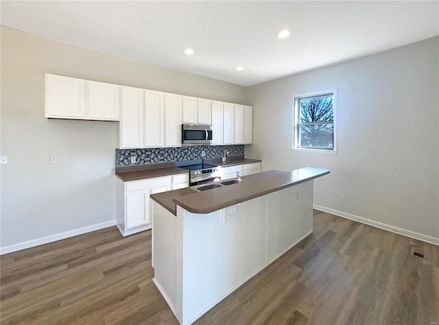 kitchen with stainless steel appliances, dark wood-type flooring, white cabinetry, dark countertops, and backsplash