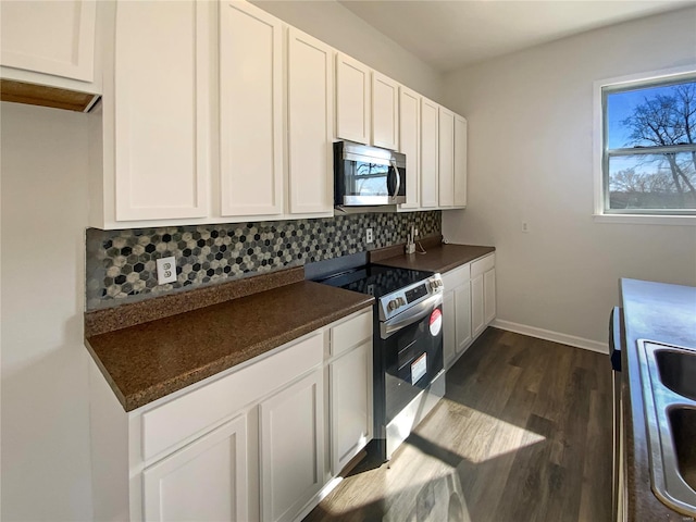 kitchen with dark countertops, backsplash, dark wood-type flooring, appliances with stainless steel finishes, and white cabinets