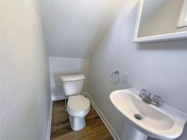 half bath featuring toilet, vaulted ceiling, wood finished floors, a textured ceiling, and a sink