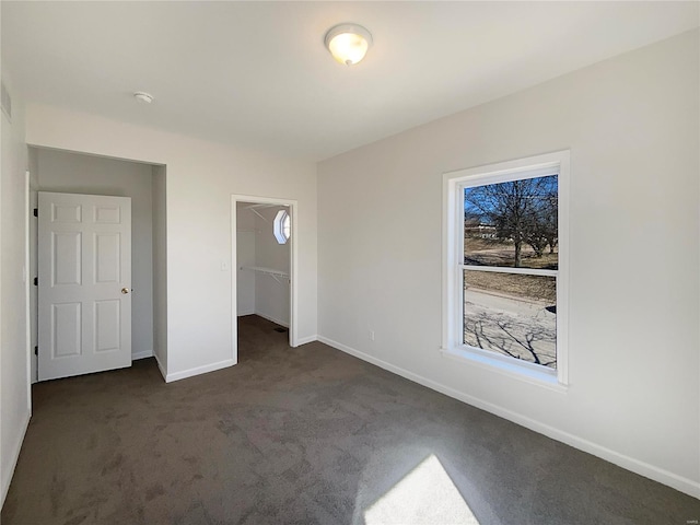 unfurnished bedroom featuring a spacious closet, baseboards, dark colored carpet, and a closet