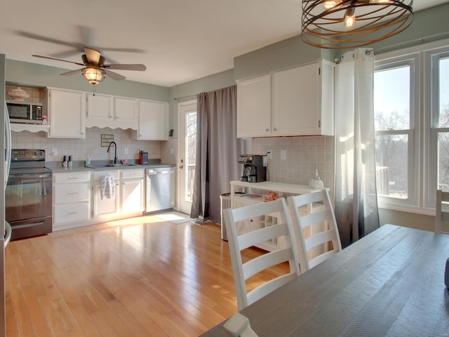 kitchen with light wood finished floors, decorative backsplash, stainless steel appliances, white cabinetry, and a sink