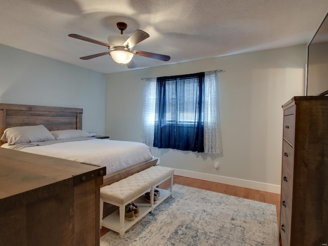 bedroom with a textured ceiling, a ceiling fan, baseboards, and wood finished floors