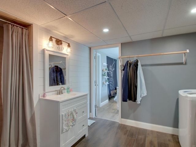 full bathroom featuring a drop ceiling, vanity, baseboards, and wood finished floors