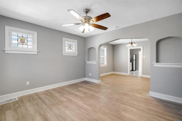 spare room featuring visible vents, ceiling fan with notable chandelier, arched walkways, light wood finished floors, and baseboards