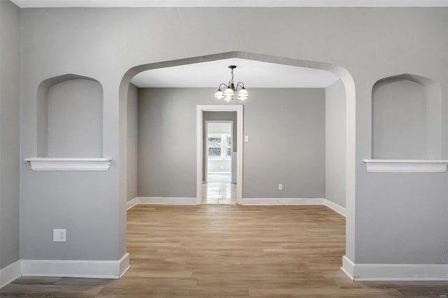 unfurnished room with light wood-type flooring, baseboards, arched walkways, and an inviting chandelier