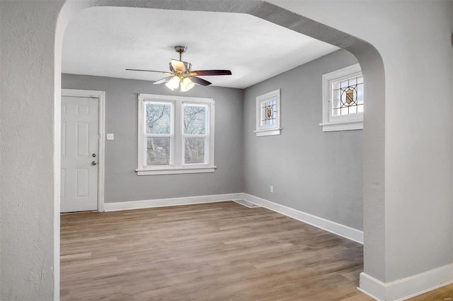 empty room with arched walkways, baseboards, and wood finished floors