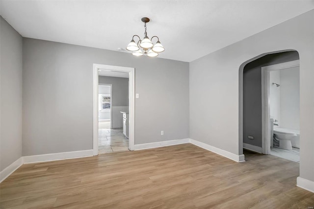 unfurnished room featuring light wood-style flooring, arched walkways, baseboards, and a chandelier