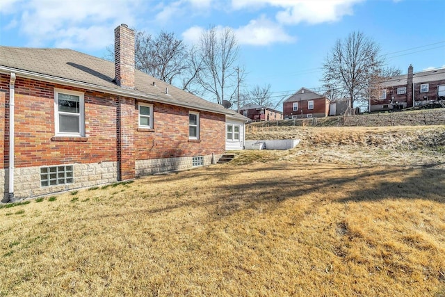 rear view of house featuring brick siding, a lawn, entry steps, and a chimney