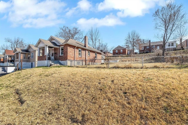 exterior space featuring a front yard, fence, a residential view, a chimney, and brick siding