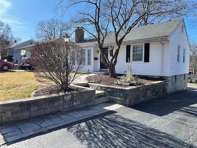 single story home with a shingled roof, a front yard, and a chimney