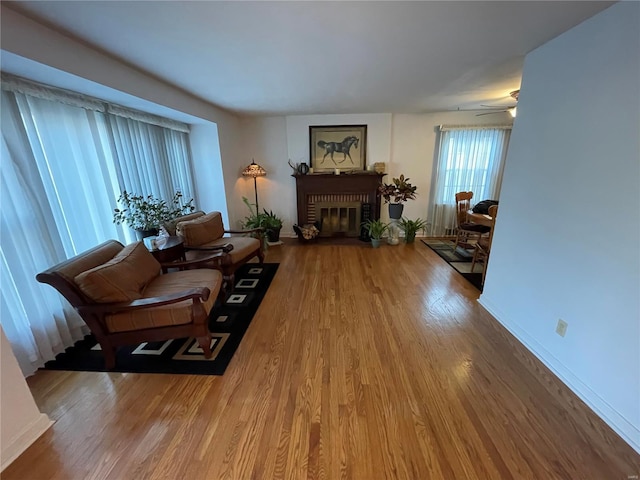 living room featuring wood finished floors, a fireplace, baseboards, and ceiling fan