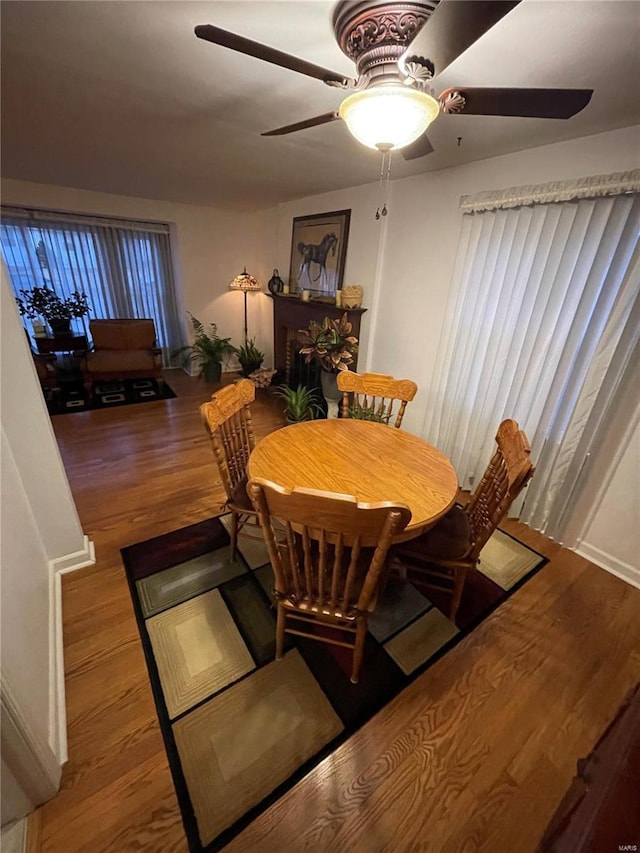 dining space featuring ceiling fan, wood finished floors, and a fireplace