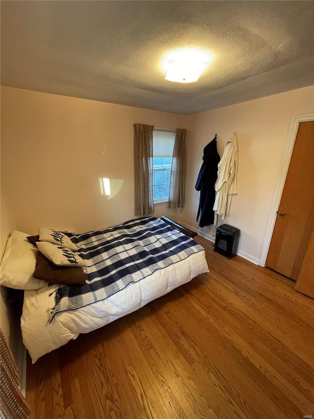 unfurnished bedroom with a textured ceiling, baseboards, and wood finished floors