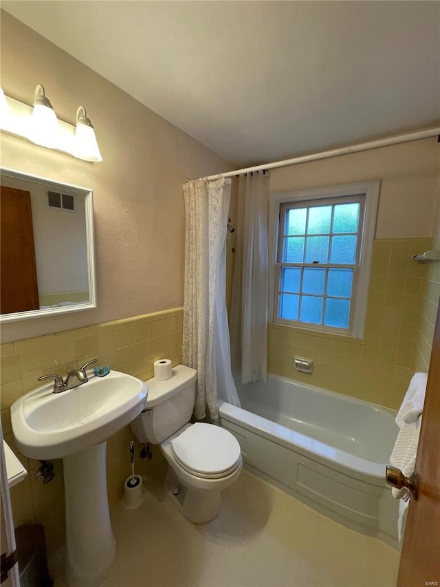 bathroom with a wainscoted wall, visible vents, shower / bath combo with shower curtain, tile walls, and toilet