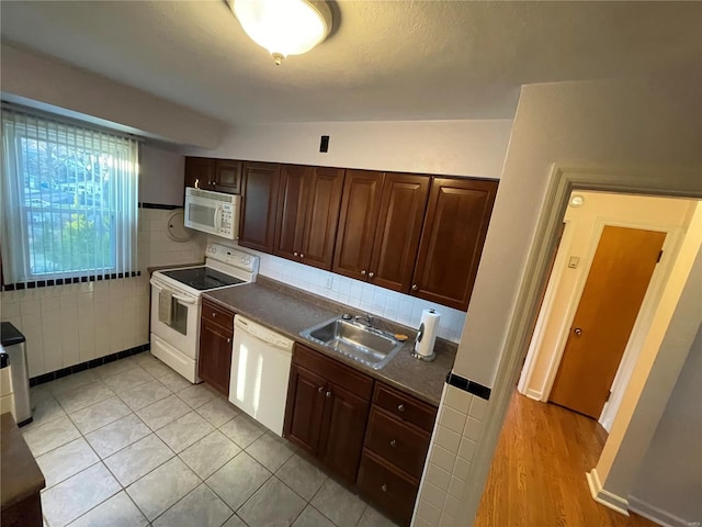 kitchen with white appliances, light tile patterned floors, a sink, dark brown cabinetry, and dark countertops