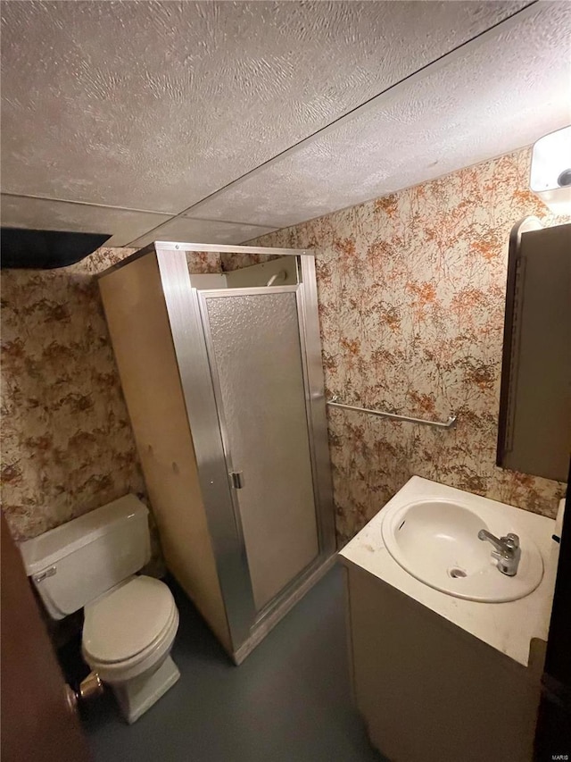 bathroom with vanity, wallpapered walls, a stall shower, a textured ceiling, and toilet