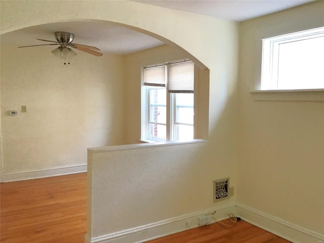 empty room with plenty of natural light, arched walkways, wood finished floors, and a ceiling fan