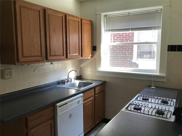 kitchen with brown cabinets, a sink, dark countertops, white appliances, and tile walls