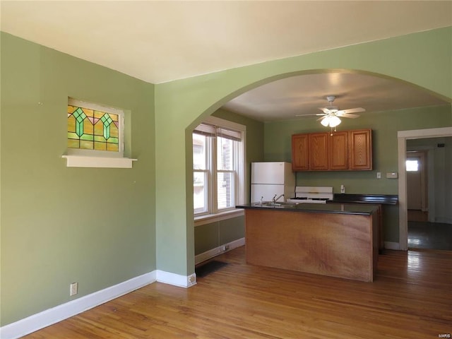 kitchen featuring dark countertops, baseboards, light wood-type flooring, brown cabinets, and freestanding refrigerator