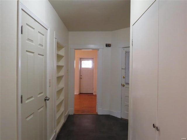 hallway with dark wood finished floors, built in shelves, and baseboards