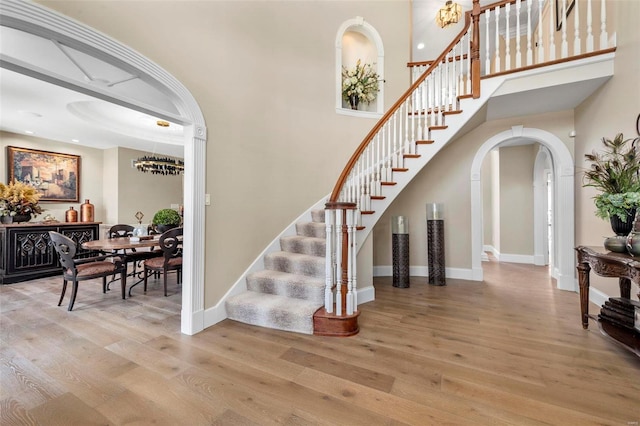 stairs with arched walkways, baseboards, and wood finished floors