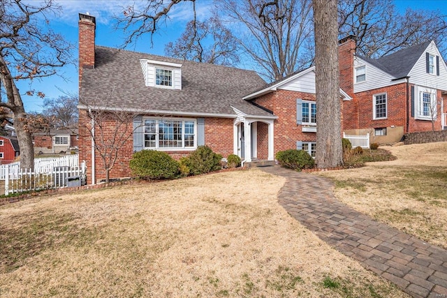 split level home featuring a front lawn, fence, a shingled roof, brick siding, and a chimney