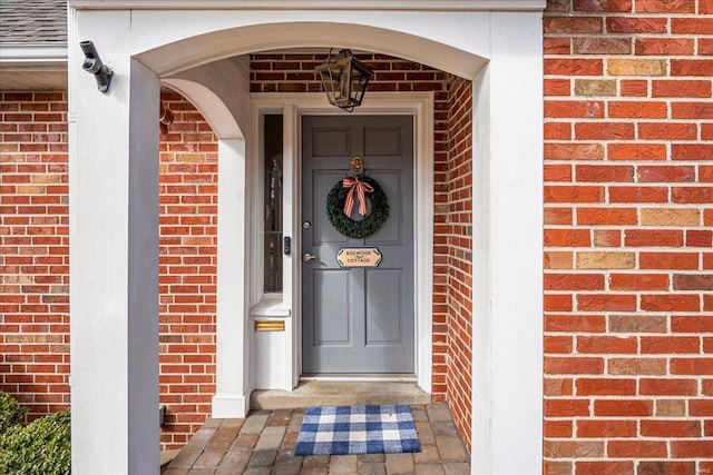 doorway to property with brick siding and a shingled roof