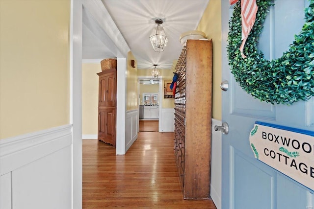 corridor with crown molding, wainscoting, an inviting chandelier, wood finished floors, and a decorative wall