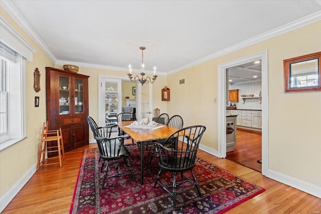 dining area with visible vents, baseboards, ornamental molding, light wood-style flooring, and an inviting chandelier