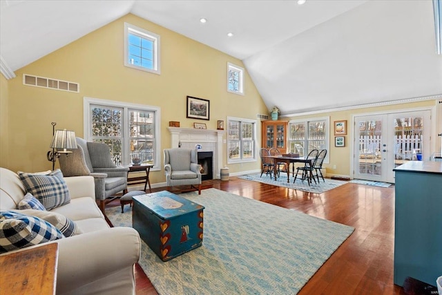 living room featuring visible vents, high vaulted ceiling, a fireplace with flush hearth, dark wood-style flooring, and french doors