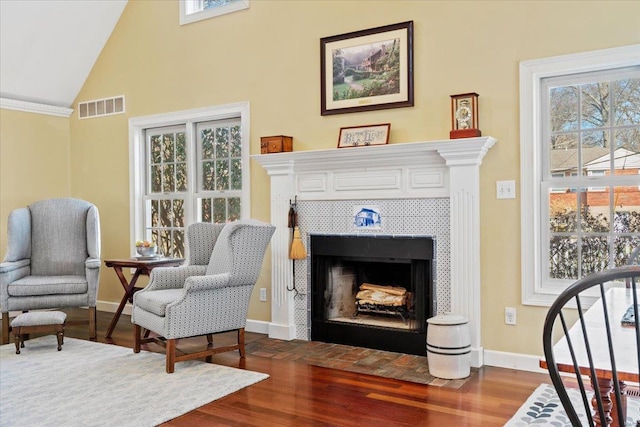 living area with visible vents, a tile fireplace, baseboards, and wood finished floors