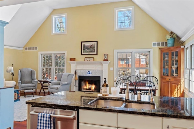 kitchen featuring visible vents, a warm lit fireplace, dark stone counters, and a sink