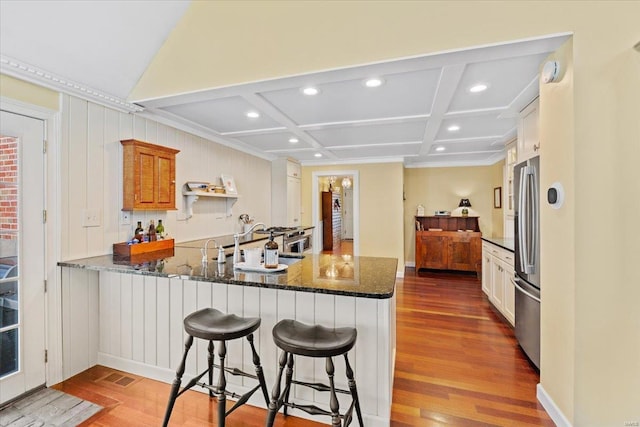 kitchen featuring dark stone counters, a kitchen bar, a peninsula, freestanding refrigerator, and coffered ceiling