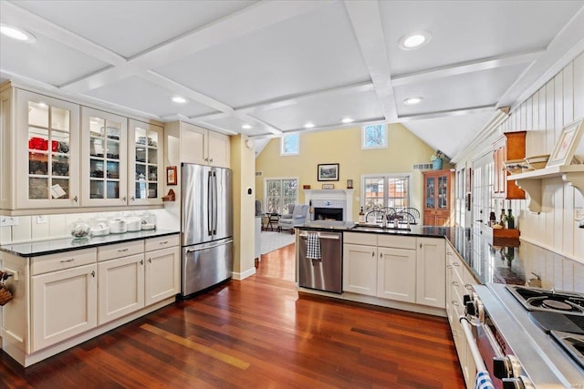 kitchen with a peninsula, dark wood-style flooring, glass insert cabinets, appliances with stainless steel finishes, and dark countertops