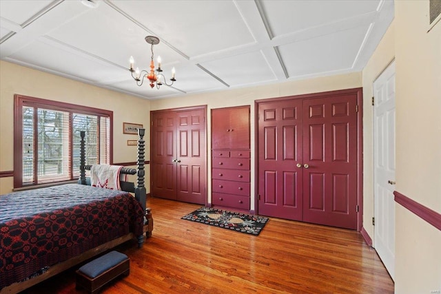 bedroom featuring a notable chandelier, multiple closets, coffered ceiling, and wood finished floors