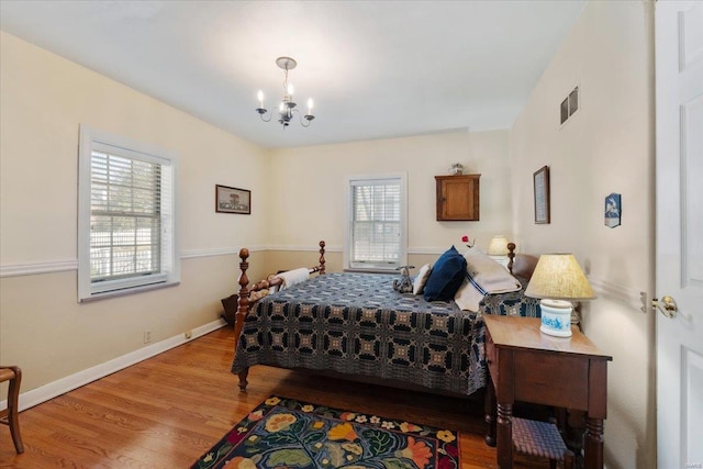 bedroom featuring a notable chandelier, visible vents, baseboards, and wood finished floors