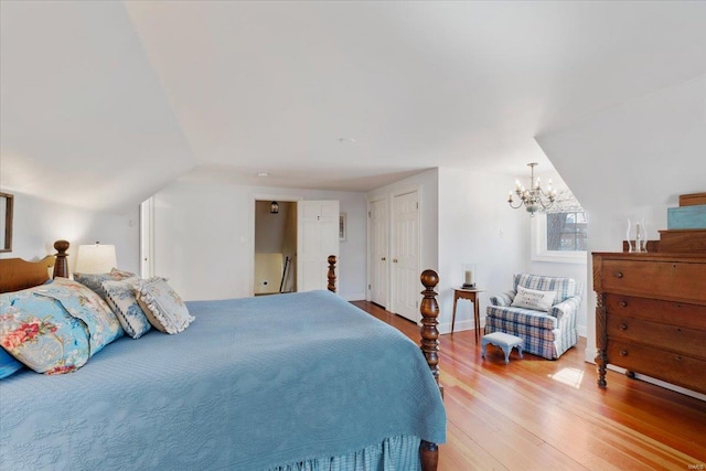 bedroom featuring baseboards, lofted ceiling, an inviting chandelier, and wood finished floors