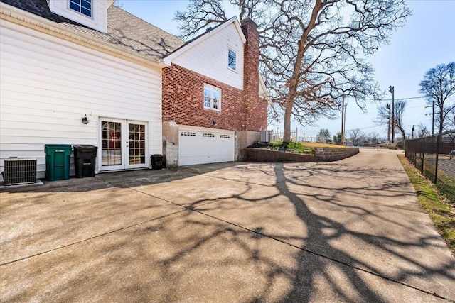 view of side of property featuring driveway, fence, cooling unit, french doors, and brick siding