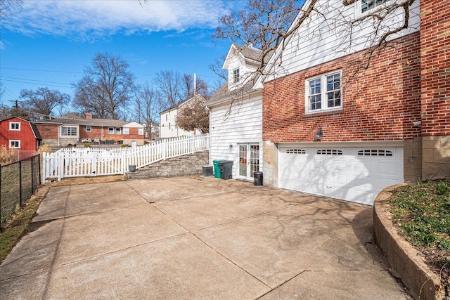 view of home's exterior with brick siding, driveway, an attached garage, and fence