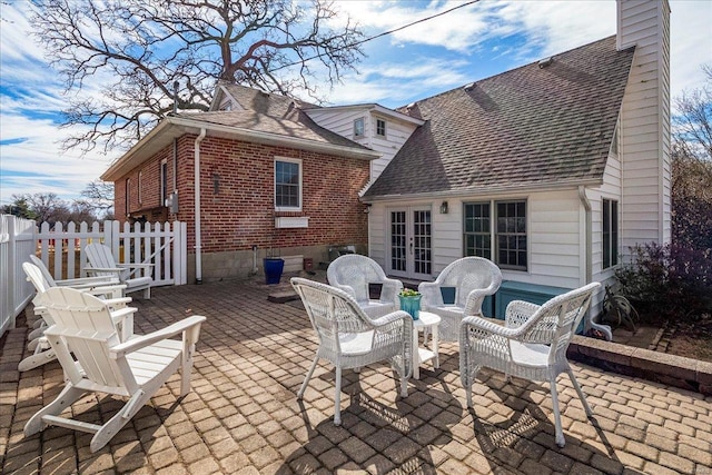 back of house with brick siding, a shingled roof, fence, french doors, and a chimney