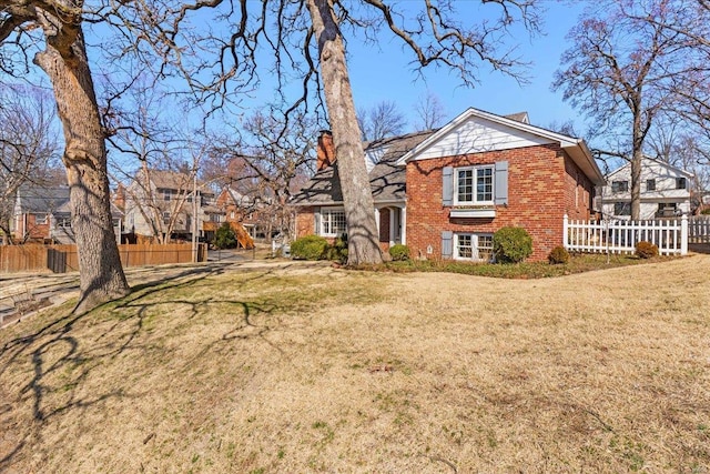 back of property featuring brick siding, a chimney, a yard, and fence