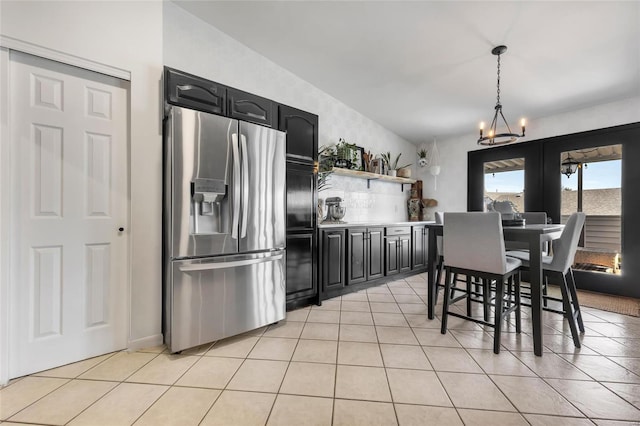 kitchen with open shelves, stainless steel fridge, an inviting chandelier, light tile patterned floors, and dark cabinets