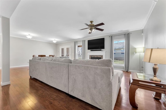 living area with dark wood-style floors, a ceiling fan, crown molding, and baseboards