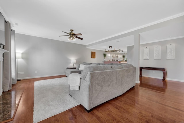 living area with a fireplace with raised hearth, crown molding, baseboards, wood finished floors, and a ceiling fan