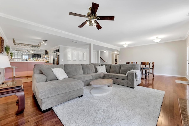 living area with baseboards, stairway, ornamental molding, a ceiling fan, and wood-type flooring