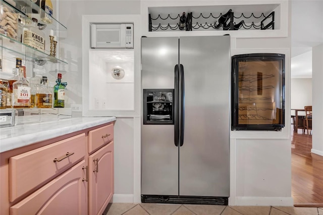 kitchen featuring light tile patterned floors, white microwave, stainless steel refrigerator with ice dispenser, and light stone countertops