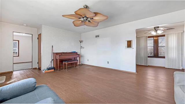 living area featuring a wood stove, baseboards, wood finished floors, and a ceiling fan