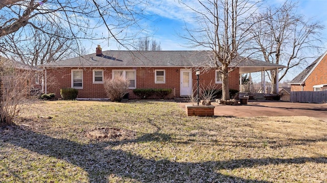 rear view of house featuring fence, a chimney, a carport, a lawn, and brick siding