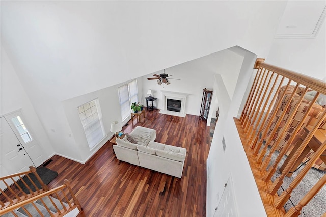 living area featuring ceiling fan, stairs, a towering ceiling, wood finished floors, and a glass covered fireplace