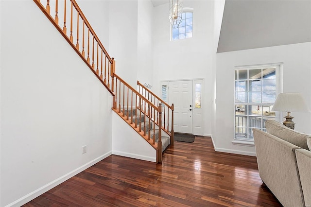 entryway with baseboards, stairs, hardwood / wood-style flooring, a towering ceiling, and a chandelier